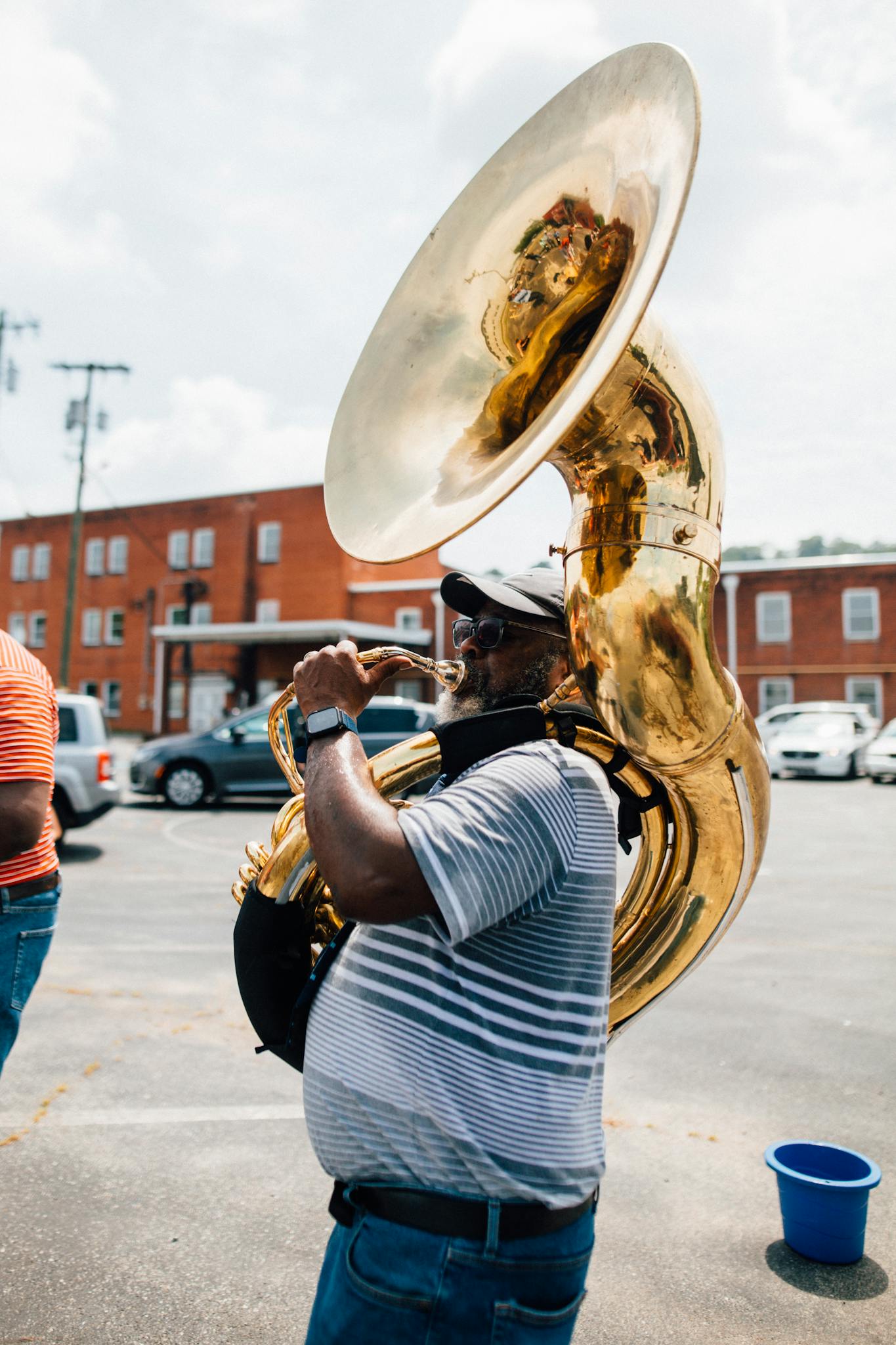 A musician performs outdoors with a sousaphone in a vibrant street scene.